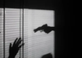 ظل شخص يحمل سلاحًا وشخص آخر يرفع يديه في وضع دفاعي.